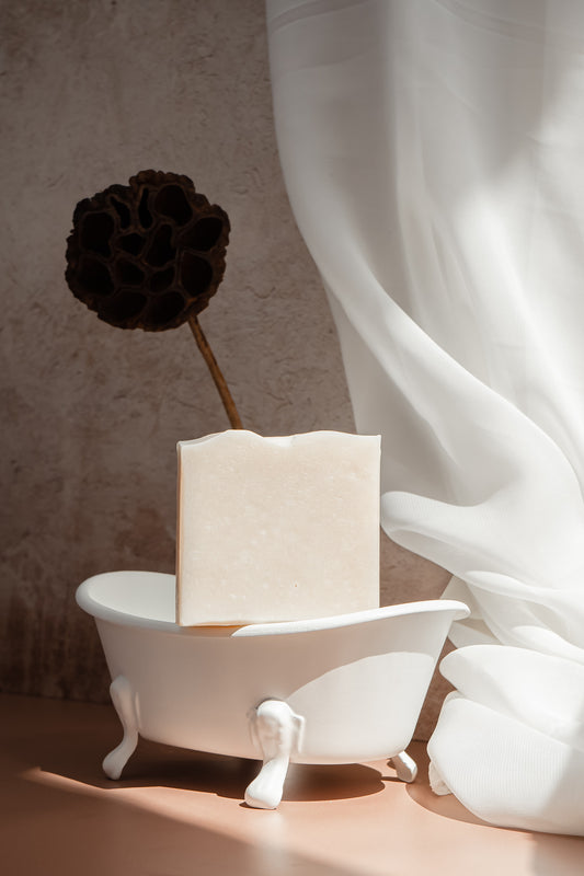 Bar of soap in a small white bathtub with a black flower on a neutral background